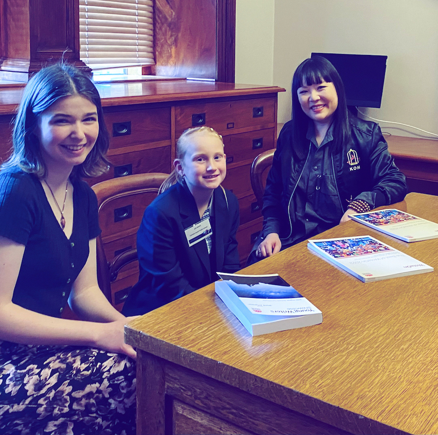 Tabitha Sharp, Zoe White and Julie Koh sitting at a table in the State Library of New South Wales with copies of the Young Writers Showcase and WriteOn anthologies in front of them.